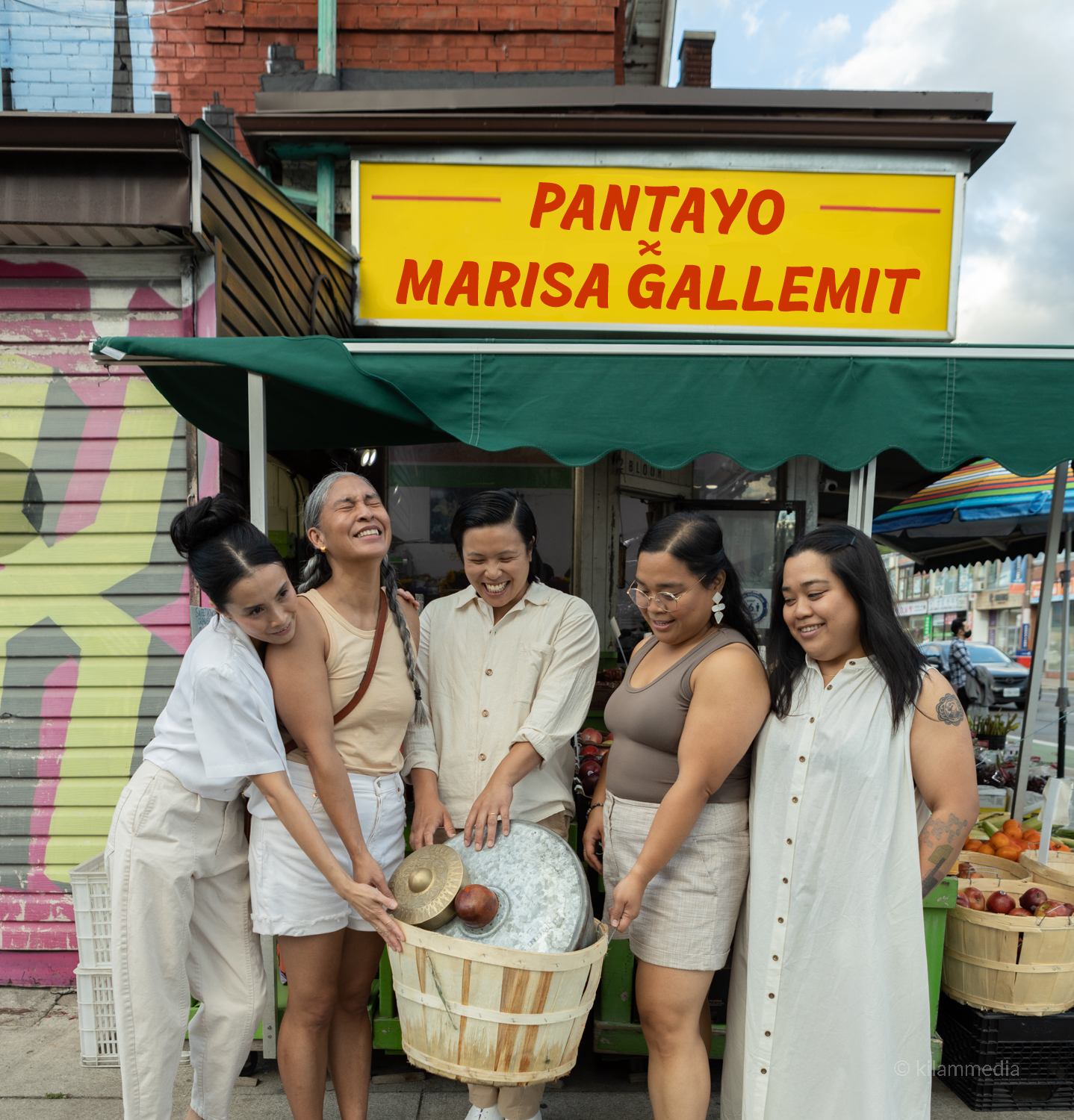 Members of Pantayo with artist Marisa Gallemit pose with a wooden basket of instruments in front of Bloor Fruit Market