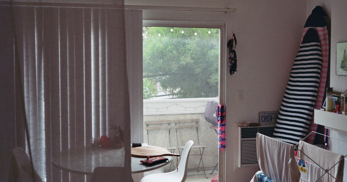Film photo of inside of apartment looking out to balcony, surfboards lean against the wall as laundry hangs to dry on a rack.
