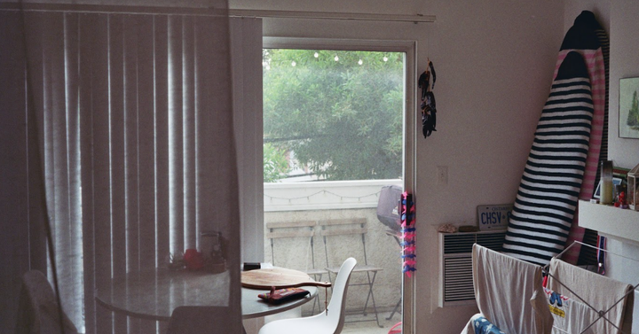 Film photo of inside of apartment looking out to balcony, surfboards lean against the wall as laundry hangs to dry on a rack.